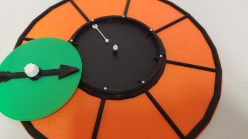 Picture of the game spinner with additional ring, spinner arrow is removed to show placement of the cog spring on one of the supports.